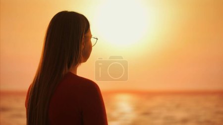 Foto de La imagen captura el perfil de una mujer reflexiva silueta contra el cautivador resplandor del sol poniente, evocando una sensación de introspección y la belleza del atardecer. - Imagen libre de derechos