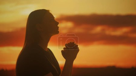 Photo for Silhouette of a young female praying folding her palms together against the bright hues of a sunset. The tranquil scene evokes a sense of peace and lightness. - Royalty Free Image