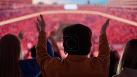 Foto de Una electrizante instantánea de los aficionados al fútbol silueta en una arena deportiva, brazos levantados en alto en celebración, cautivados por la acción en el estadio, inmersos en la pasión compartida del momento. - Imagen libre de derechos