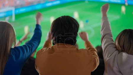Téléchargez les photos : Un instantané électrisant des fans de soccer silhouette dans une arène sportive, les bras levés haut dans la célébration, captivé par l'action sur le stade, immergé dans la passion partagée du moment. - en image libre de droit