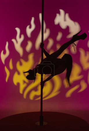 Foto de Silueta de una hermosa mujer sexy realiza elementos de baile erótico polo. Bailarina femenina realiza coreografía exótica sobre pilón en estudio. - Imagen libre de derechos
