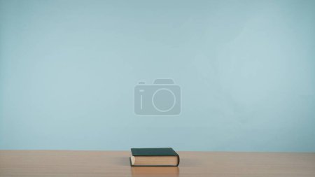 Foto de Un libro sobre una mesa de madera sobre un relajante fondo azul pastel. Un homenaje al encanto atemporal de la lectura y el conocimiento. Ficción.. - Imagen libre de derechos