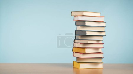 Foto de Una colección de una imponente pila de libros antiguos sobre una mesa de madera sobre un relajante fondo azul pastel. Un homenaje al encanto atemporal de la lectura y el conocimiento. Ficción.. - Imagen libre de derechos