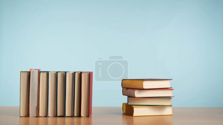 Foto de Una fila de libros sobre una mesa de madera sobre un relajante fondo azul pastel. Un homenaje al encanto atemporal de la lectura y el conocimiento. Ficción.. - Imagen libre de derechos