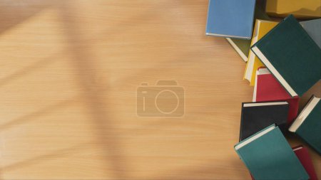 Foto de Montón de libros antiguos con cubiertas de colores en una mesa de madera sobre un fondo naranja brillante. Un homenaje al encanto atemporal de la lectura y el conocimiento. Ficción.. - Imagen libre de derechos