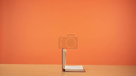 Photo for An old open book with red cover on a wooden table on a bright orange background. A tribute to the timeless allure of reading and knowledge. Fiction. - Royalty Free Image