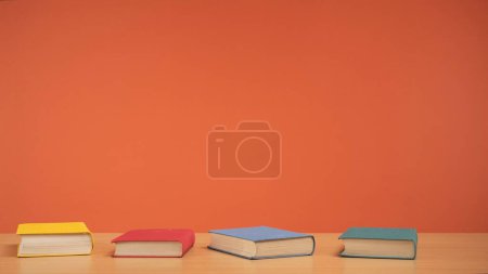Photo for Old books with colored covers on a wooden table on a bright orange background. A tribute to the timeless allure of reading and knowledge. Fiction. - Royalty Free Image