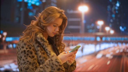 Photo for Gadgets and modern everyday life advertisement concept. Female using smartphone on daily basis. Young woman on the street at night texting messaging on smartphone with friends, going to party. - Royalty Free Image