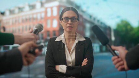 Photo for Live tv news broadcasting concept. Female expert answering questions.. People journalists news reporters taking interview with woman outdoors, reporting on air, city downtown background at the back. - Royalty Free Image