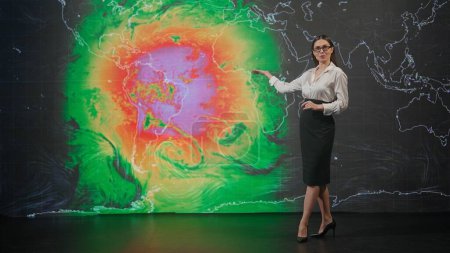 Live tv news broadcasting concept. Female presenter in the studio. Woman anchor news host presenting weather forecast, reporting on air, virtual climate map graphic background at the back.