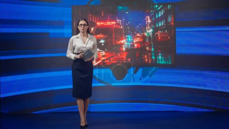 Photo for Live tv news broadcasting concept. Female presenter in the studio. Woman news host presenting breaking event, reporting about catastrophe on air, tragedy scene graphic background at the back. - Royalty Free Image
