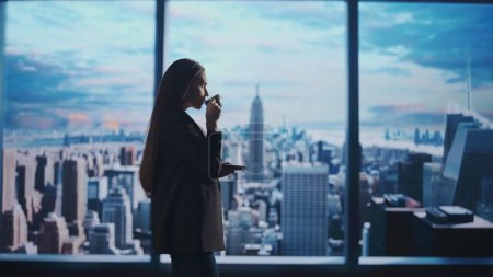 Photo for Corporate business advertisement concept. Successful business woman in the office. Woman ceo hedge fund top manager drinking coffee from a mug in front of window with morning city view. - Royalty Free Image