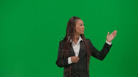 Téléchargez les photos : Reportage TV et concept de publicité de diffusion en direct. Rapporteuse isolée sur fond vert chroma key. afro-américaine femme news hôte en costume parler montrant à vide espace. - en image libre de droit