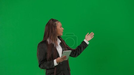 Photo for Tv news report live broadcasting advertisement concept. Female reporter isolated on chroma key green screen background. African American woman news host in suit with tablet talking shows empty area. - Royalty Free Image