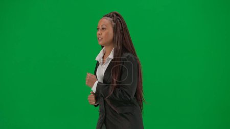 Photo for Tv news report and live broadcasting advertisement concept. Female reporter isolated on chroma key green screen background. African American woman news host presenter in suit runs in front of camera - Royalty Free Image