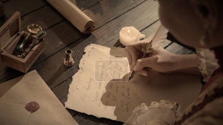 Photo for Historical letter creative concept. Female in antique outfit writes with feather pen. Shot of woman writing a letter with vintage quill feather pen on old parchment paper at the desk. - Royalty Free Image