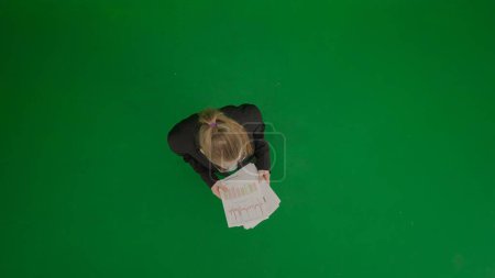 Modern businesswoman creative advertisement concept. Portrait of female in suit on chroma key green screen. Blonde business woman in formal outfit holding paper. Top view.