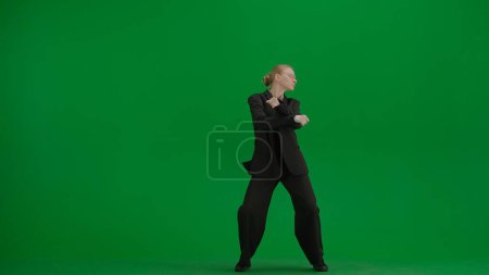 Téléchargez les photos : Femme en costume d'affaires noir dansant joyeusement sur écran vert avec chromakey. Concept publicitaire créatif femme d'affaires moderne. - en image libre de droit