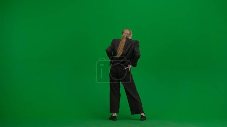 Frau im schwarzen Business-Anzug tanzt fröhlich auf grünem Bildschirm mit Chromakey. Moderne Geschäftsfrau kreatives Werbekonzept.