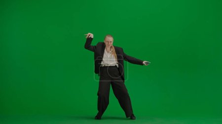 Frau im schwarzen Business-Anzug tanzt fröhlich auf grünem Bildschirm mit Chromakey. Moderne Geschäftsfrau kreatives Werbekonzept.