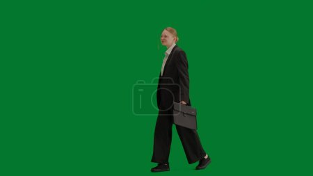 Téléchargez les photos : Concept moderne de publicité créative femme d'affaires. Portrait de femme en costume sur écran vert chromé. Femme d'affaires blonde en tenue formelle marchant avec mallette. - en image libre de droit