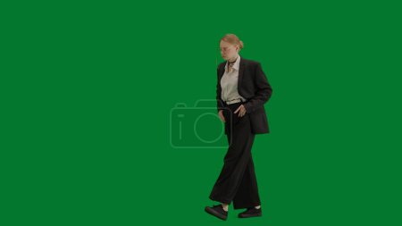 Téléchargez les photos : Concept moderne de publicité créative femme d'affaires. Portrait de femme en costume sur écran vert chromé. Femme d'affaires blonde en tenue formelle marche et danse, expression positive souriante. - en image libre de droit