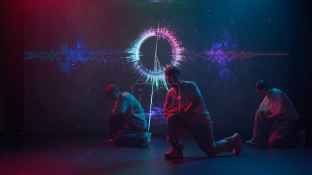 In a modern studio bathed in the glow of a large LED screen, a trio of dancers two women and one man showcase their hip-hop skills. The screen behind them flickers with vibrant dynamic backgrounds.