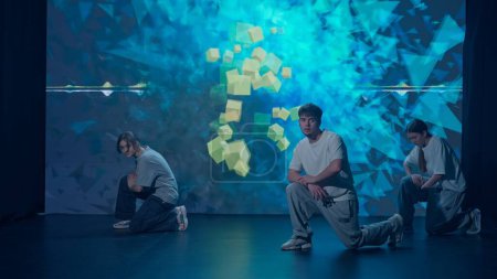 En un estudio moderno bañado en el resplandor de una pantalla led grande, un trío de bailarines dos mujeres y un hombre exhiben sus habilidades del hip-hop. La pantalla detrás de ellos parpadea con fondos dinámicos vibrantes.