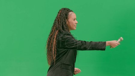 Tv news and live broadcasting concept. Young female reporter isolated on chroma key green screen background. African american woman tv news host taking interview using microphone.