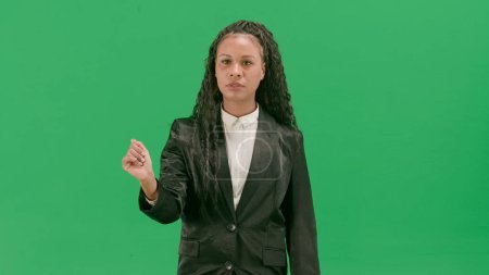 Tv news and live broadcasting concept. Young female reporter isolated on chroma key green screen background. African american woman tv news host uses virtual screen, swiping gesture.