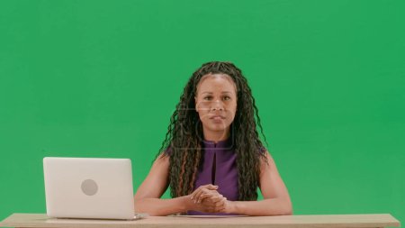 Téléchargez les photos : Nouvelles TV et concept de diffusion en direct. Femme en robe assis au bureau isolé sur fond d'écran vert clé chroma. afro-américaine femme tv nouvelles hôte assis parler caméra. - en image libre de droit