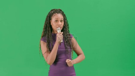 Photo for Tv news and live broadcasting concept. Female in dress isolated on chroma key green screen background. African american woman tv news host standing talking in microphone looking at camera. - Royalty Free Image