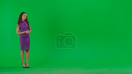 Téléchargez les photos : Nouvelles TV et concept de diffusion en direct. Femme en robe isolée sur fond vert chroma key. Plein plan afro-américaine femme tv nouvelles hôte debout parler regardant caméra. - en image libre de droit