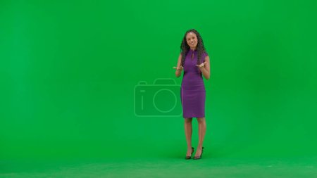 Tv news and live broadcasting concept. Female in dress isolated on chroma key green screen background. Full shot african american woman tv news host standing talking looking at camera.