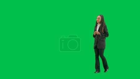Photo for Tv news and live broadcasting concept. Young female reporter isolated on chroma key green screen background. Full shot african american woman tv news host walking and talking. Half turn. - Royalty Free Image