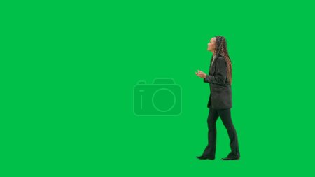 Photo for Tv news and live broadcasting concept. Young female reporter isolated on chroma key green screen background. Full shot african american woman tv news host walking and talking. Side view. - Royalty Free Image