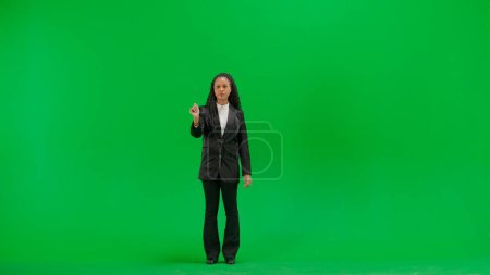 Tv news and live broadcasting concept. Young female reporter isolated on chroma key green screen background. Full shot african american woman tv news host uses virtual screen, swiping gesture.