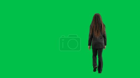 Photo for Tv news and live broadcasting concept. Young female reporter isolated on chroma key green screen background. Full shot african american woman tv news host walking. Back view. - Royalty Free Image