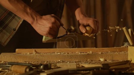 Photo for Carpentry and handicraft advertisement concept. Male woodworker working in garage. Man professional carpenter specialist working with wooden materials in workshop, planes the plank. - Royalty Free Image