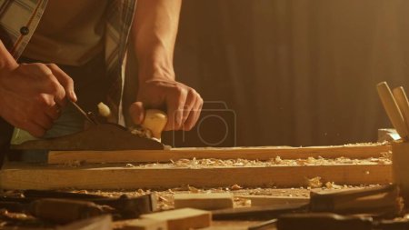 Photo for Carpentry and handicraft advertisement concept. Male woodworker working in garage. Man professional carpenter specialist working with wooden materials in workshop, planes the plank. - Royalty Free Image