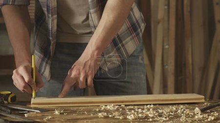 Carpentry and handicraft advertisement concept. Male woodworker working in garage. Man professional carpenter working with wooden materials in workshop and makes pencil markings.