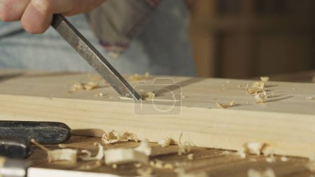 Téléchargez les photos : Menuiserie et artisanat concept de publicité. Travailleur du bois dans le garage. Homme menuisier professionnel travaillant avec des meubles en bois en atelier, sculptant le bois à l'aide d'un ciseau. - en image libre de droit