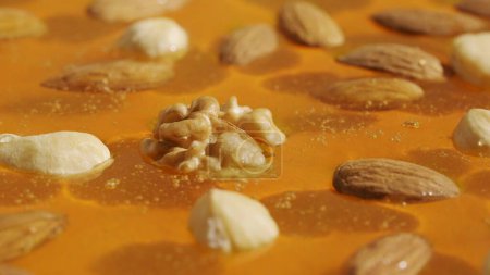 Photo for Food advertisement concept. Healthy organic honey. Sweet fresh golden honey on the yellow background, almonds walnuts and cashew nuts in the thick syrup, close up shot. - Royalty Free Image