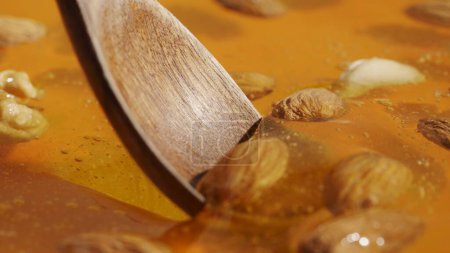 Foto de Concepto de publicidad de alimentos. Miel orgánica saludable. Dulce miel dorada fresca en el fondo amarillo, cuchara de madera recogiendo almendras nueces y nueces de anacardo cubierto con el jarabe grueso, tiro de cerca. - Imagen libre de derechos