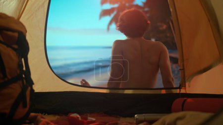 Téléchargez les photos : Concept camping et aventure. Homme se reposant sur le camping relaxant près de l'océan. Jeune homme assis devant la tente au coucher du soleil sur la plage regardant la mer, vacances en plein air. - en image libre de droit