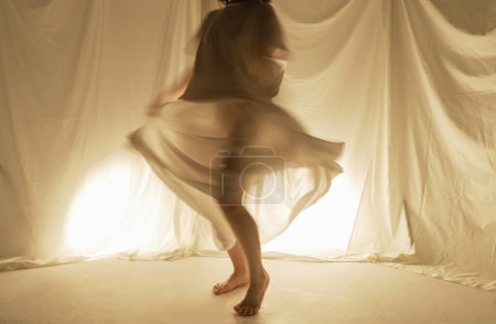Téléchargez les photos : Une silhouette de danseuse tournoie, sa jupe gonfle, dans une pièce éclairée par un contre-jour chaleureux. - en image libre de droit
