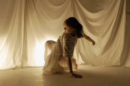 Foto de La silueta de una bailarina bailando en el suelo sobre un fondo claro es capturada en movimiento por telas que fluyen. - Imagen libre de derechos