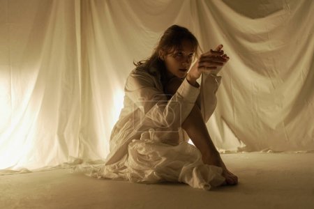 Foto de La silueta de una bailarina bailando en el suelo sobre un fondo claro es capturada en movimiento por telas que fluyen. - Imagen libre de derechos