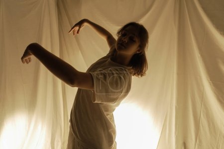 Téléchargez les photos : Silhouette d'une danseuse sur fond clair, capturée en plein mouvement avec des tissus fluides. - en image libre de droit