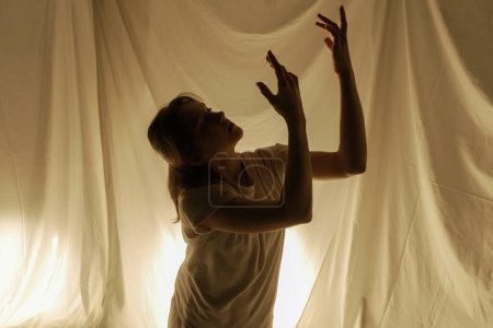 Téléchargez les photos : Silhouette d'une danseuse sur fond clair, capturée en plein mouvement avec des tissus fluides. - en image libre de droit
